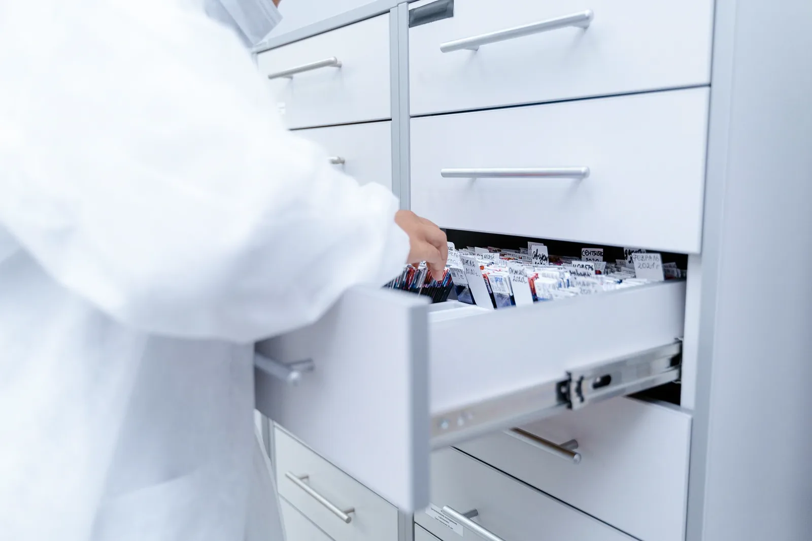 A lab technician in a white coat pulling open a drawer of catalogued records.